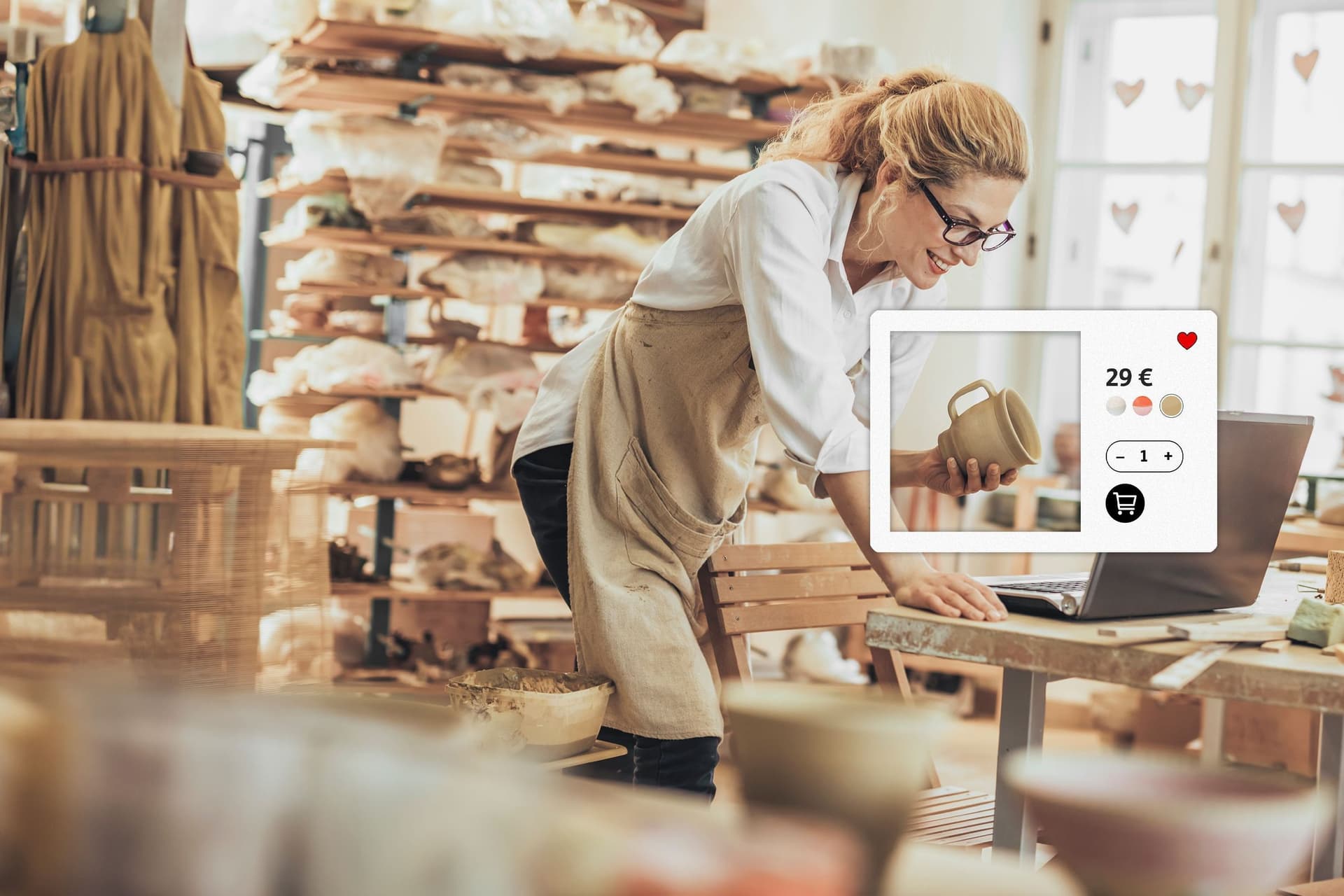 Eine Frau in einer Töpferei beugt sich über einen Laptop und hält ein getöpfertes Gefäß in der Hand.